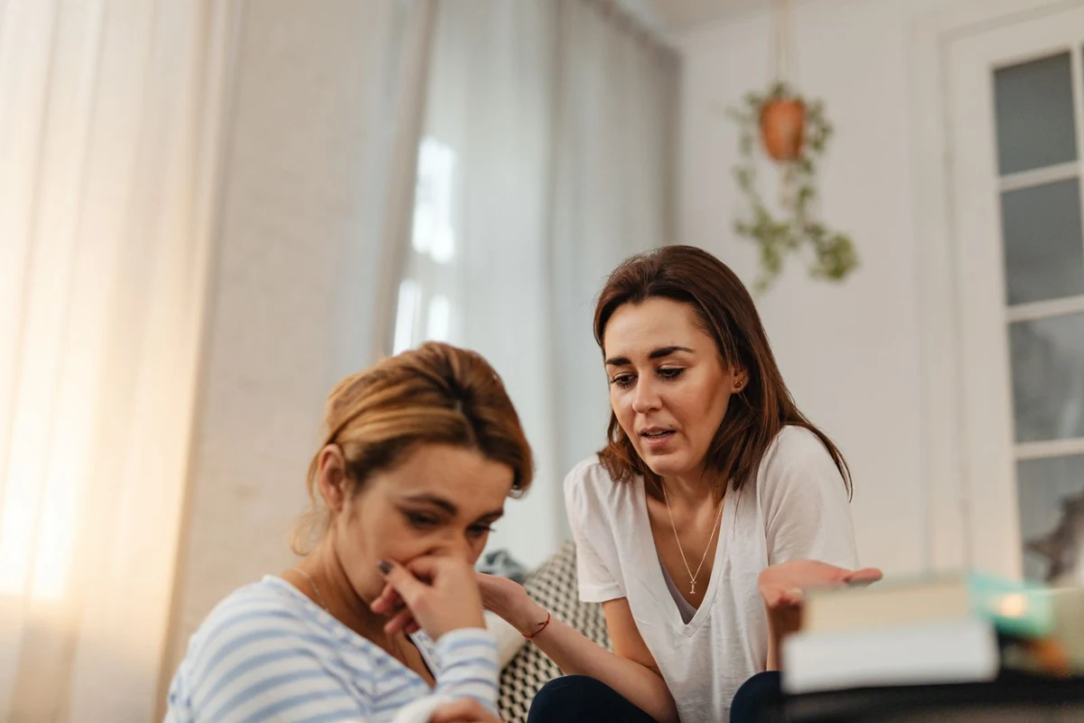 Una mujer consuela a su amiga, sentadas frente a frente en casa