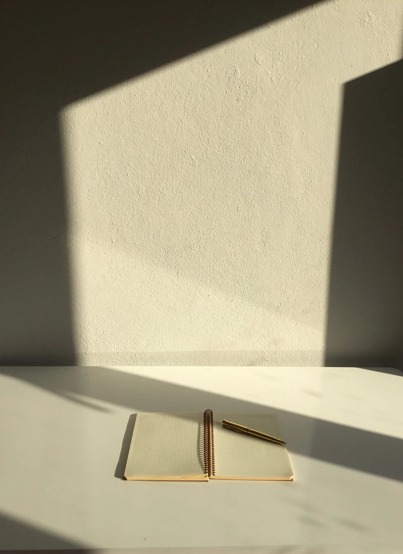 Un cuaderno en blanco sobre una mesa, con la luz de la ventana marcando una sombra diagonal
