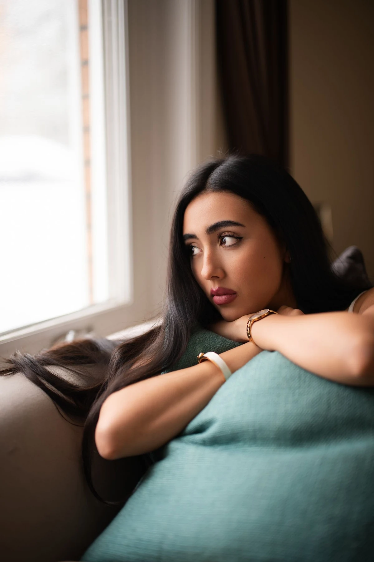 Mujer sentada junto a una ventana, apoyada sobre una mano